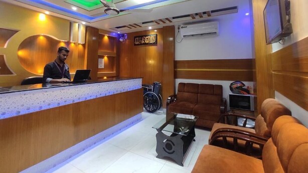 Zona de recepción con mostrador de madera, una silla de ruedas, un sofá y un televisor montado en la pared.