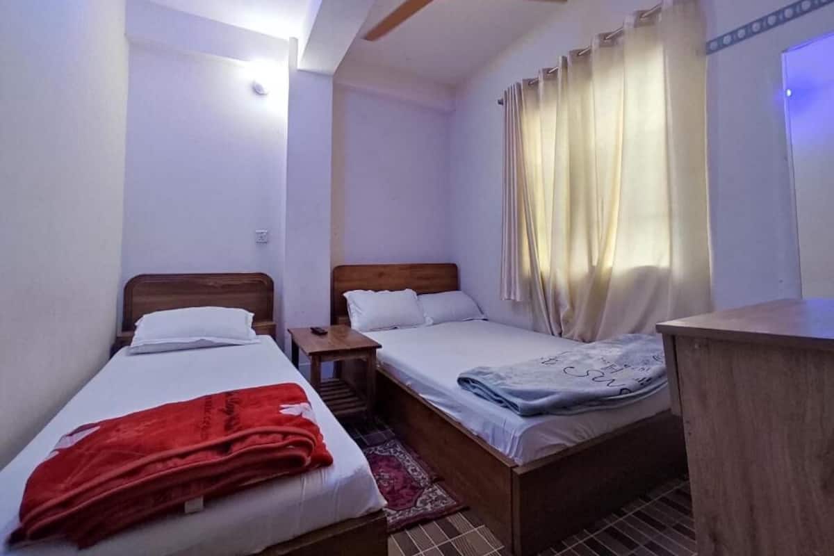 Une petite pièce bien éclairée, avec deux lits simples, un bureau et un ventilateur de plafond.