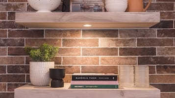 A shelf with a plant, books, and decorative items against a brick wall.