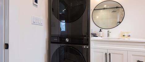 A modern bathroom with a black washing machine, a round mirror, and a white vanity with cabinets.