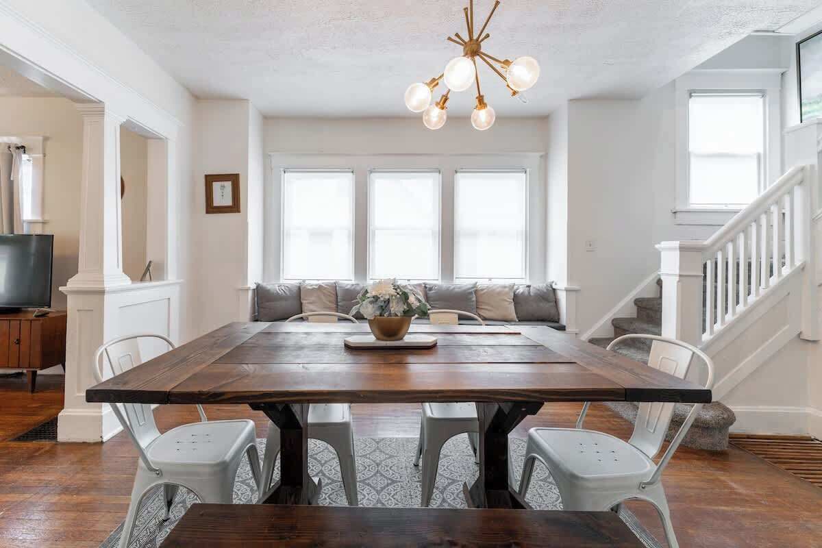 Un espace repas avec une grande table en bois, des chaises blanches et un lustre.
