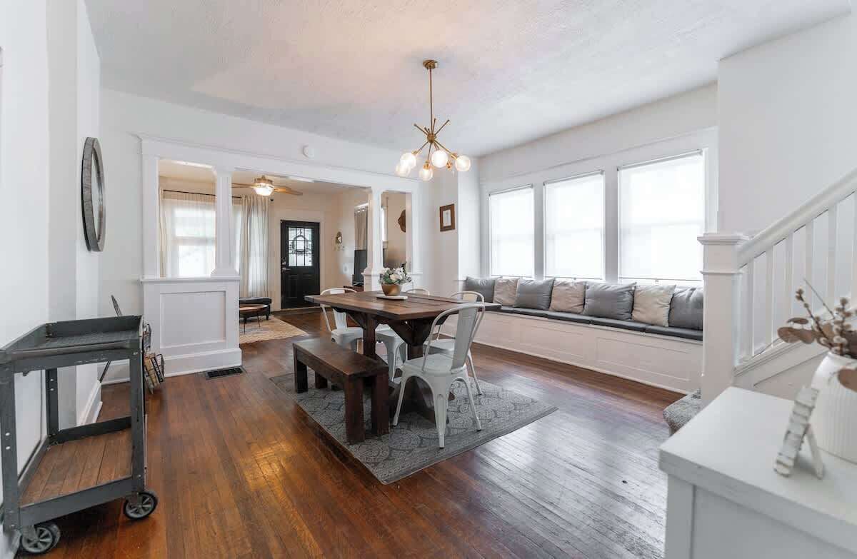Un salon spacieux doté d’un plancher en bois, un coin repas avec une table et des chaises, un banc et une grande fenêtre offrant une vue dégagée.