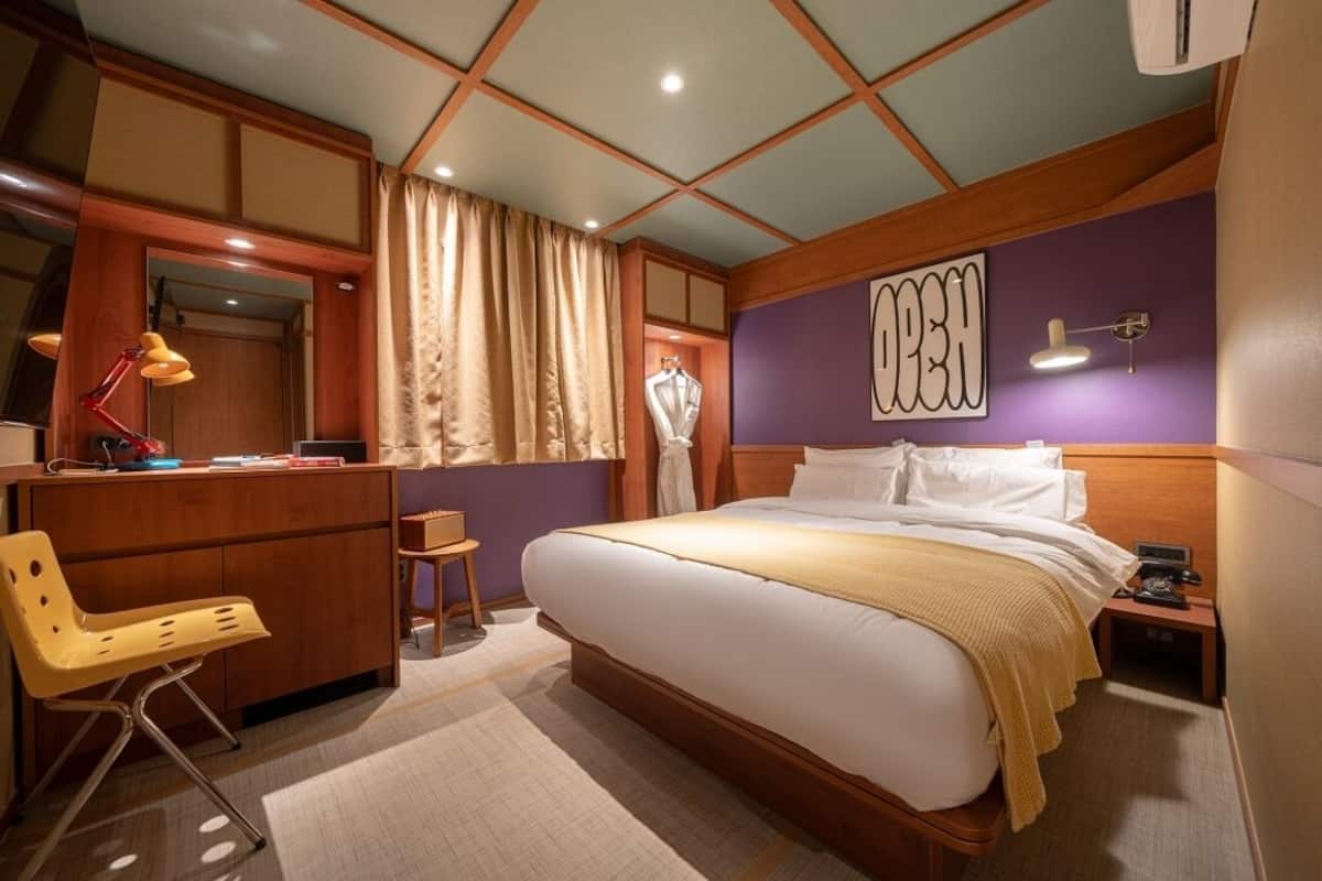 A hotel room with a large bed, a desk with a chair, a wardrobe, and a vanity with a mirror.