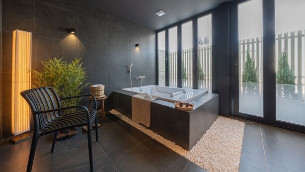 A modern bathroom with a large bathtub, a chair, a plant, and a view of the outdoors. - Anook Ryokan Yosuriguri Hotel (Cheonan)