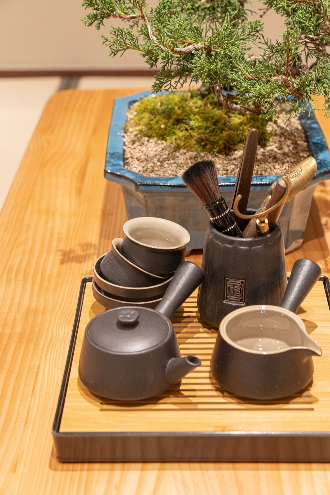 A traditional tea set with a teapot, cups, and a brush on a wooden tray.