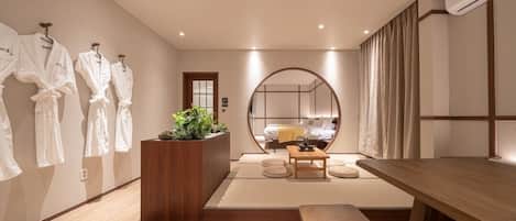 Una habitación de hotel moderna con un espejo grande, un banco de madera, una mesita pequeña y una planta.