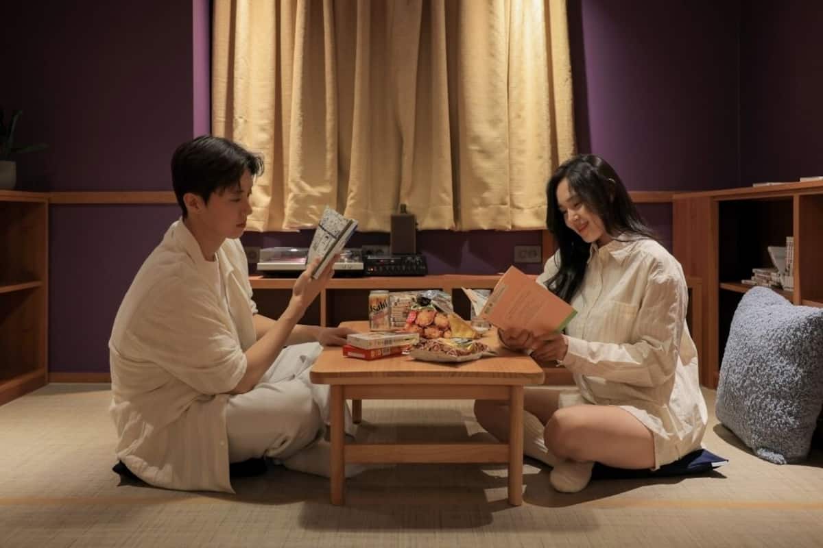 Two people sitting on the floor, reading books, with a table in front of them containing food and drinks.