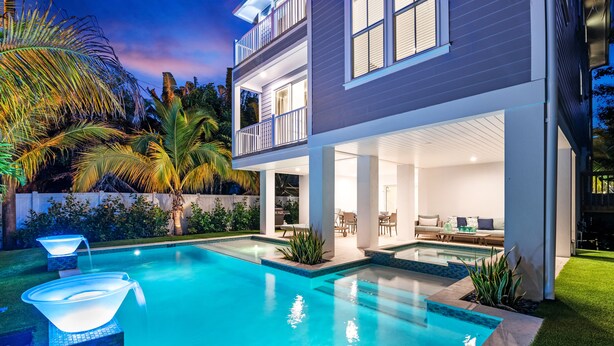 Una casa moderna de dos pisos con piscina, mobiliario exterior y un patio bien iluminado.