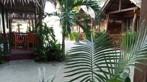 A beachside area with thatched-roof structures, outdoor seating, and tropical plants. - Zhaya's Beach and Cottages (El Nido)