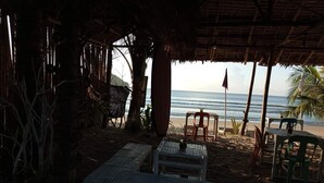 A beachside hut with a thatched roof, a wooden table, and chairs. - Zhaya's Beach and Cottages (El Nido)