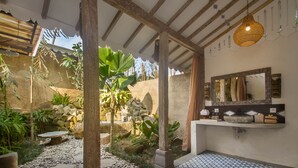A bathroom with a patterned tile floor, a stone wall, a wooden bench, and a hanging light fixture. -  Sacred Beji by GenuineHost (Payangan)