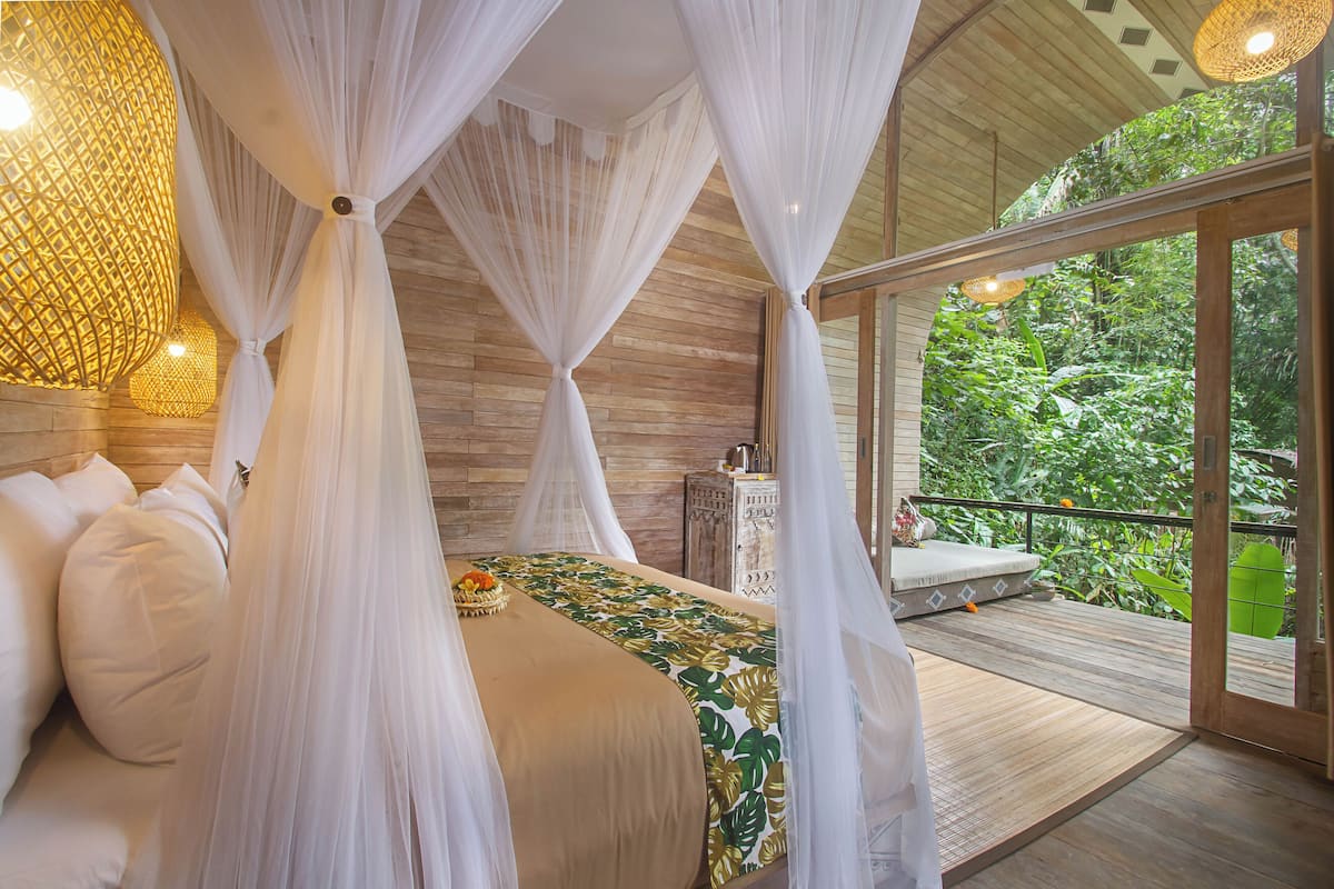 Un dormitorio con cama con dosel, suelo de madera y vistas a exuberante vegetación.