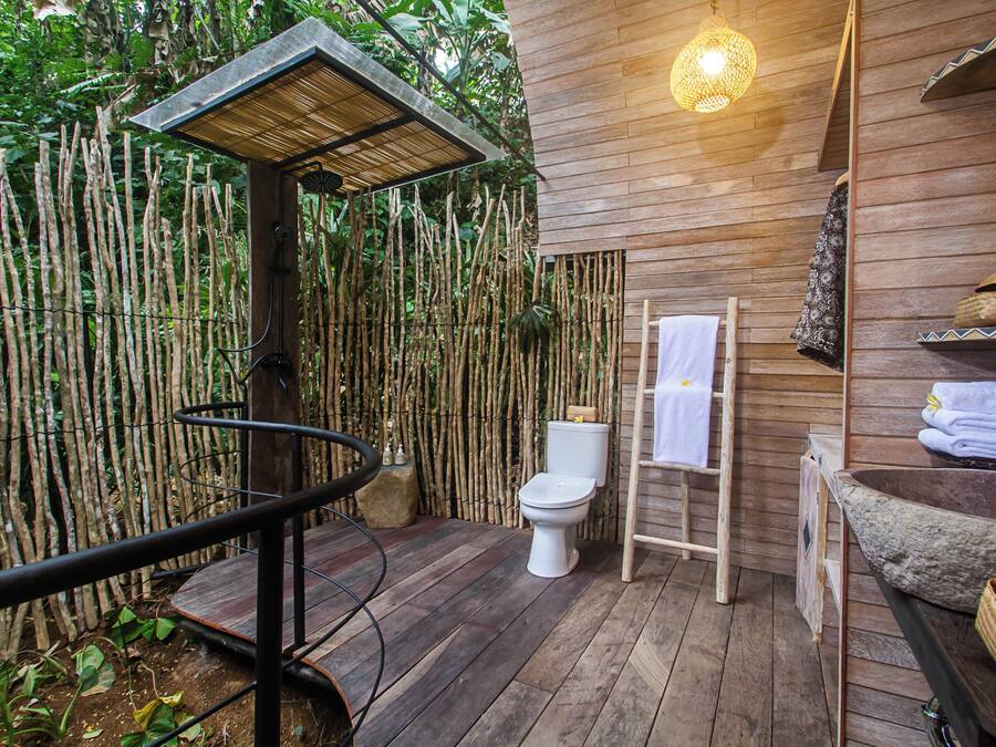 Un bagno con pareti in bambù, dotato di un water, un lavabo in legno e una zona doccia.
