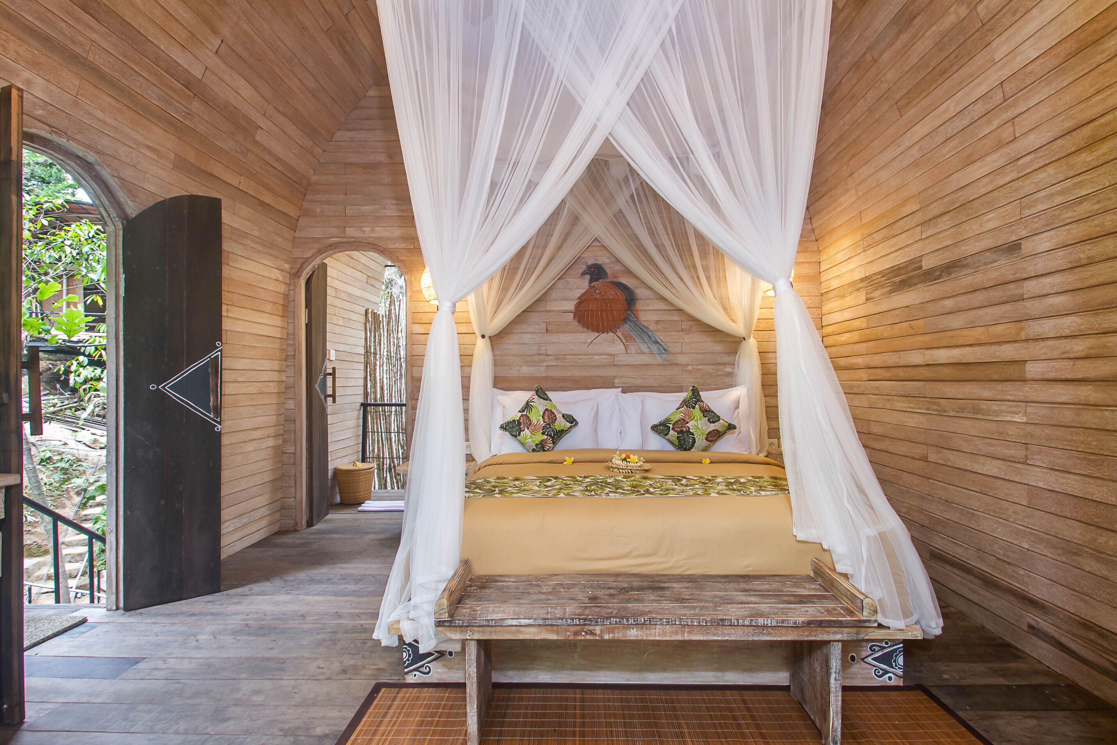 Ein Zimmer mit Holzboden, einem Himmelbett und einer an der Wand befestigten Vogel-Skulptur.