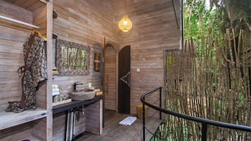Interior de madera con un banco de madera, un colgante de luz y vistas a un bosque de bambú.