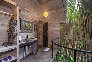 Interior de madera con un banco de madera, un colgante de luz y vistas a un bosque de bambú.