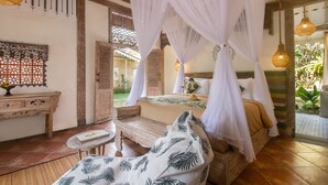 A bedroom with a canopy bed, a wooden bench, a small table, and a decorative wall piece. -  Sacred Beji by GenuineHost (Payangan)