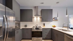 A modern kitchen with stainless steel appliances, grey cabinets, and a central island. - Savanna-Odyssey at the Park- Pool & Full Gym (Nashville)