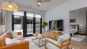 A modern living room with a sofa, coffee table, TV, and a balcony view. - Savanna-Odyssey at the Park- Pool & Full Gym (Nashville)