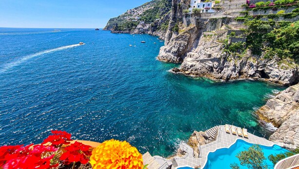Vista costera con mar azul transparente, un acantilado rocoso y una piscina.