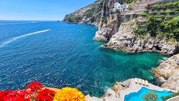 Vista sulla costa con un mare blu limpido, una scogliera rocciosa e una piscina.