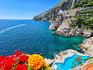 Vista costera con mar azul transparente, un acantilado rocoso y una piscina.
