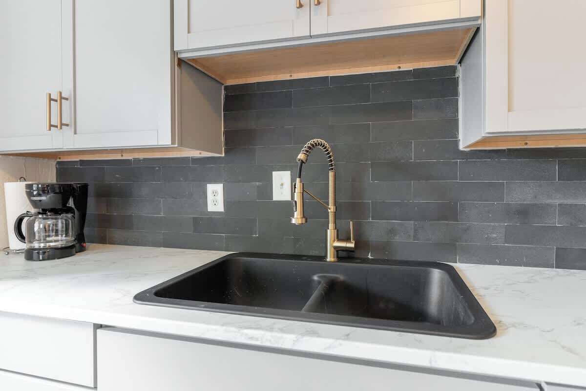 A kitchen with a black tiled backsplash, a stainless steel sink, and a coffee maker on the counter.
