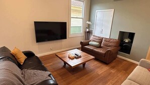 Una sala de estar con televisión de pantalla plana, sofás de cuero, una mesa de centro de madera y chimenea.