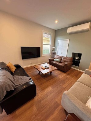 A living room with a flat-screen TV, leather sofas, a wooden coffee table, and a fireplace. - Altam House, Ballarat Central (Ballarat Central)