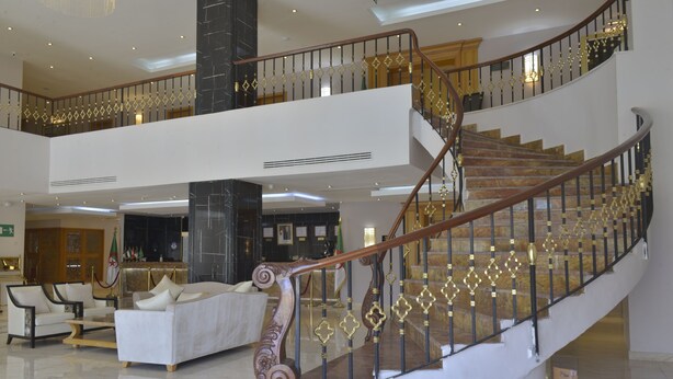 Un magnifique escalier orné de balustrades travaillées, un coin salon confortable avec un canapé et des fauteuils, et un plafond haut doté d’un éclairage encastré.