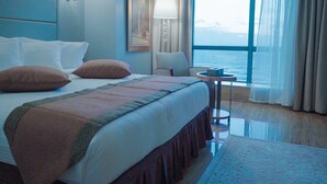 Une chambre d’hôtel avec un grand lit, une petite table ronde et une vue sur la mer par la fenêtre.