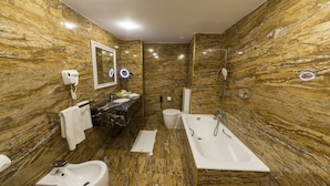 Une salle de bain avec des murs en marbre, un lavabo, un bidet, des toilettes et une baignoire.