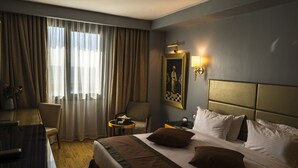 Une chambre d’hôtel avec un lit, un bureau, une chaise, une petite table et un tableau au mur.