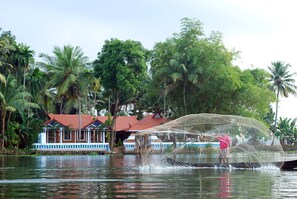 A house with a red roof and blue trim, surrounded by lush greenery and palm trees. - The Lake Resort by Maat Hotels (Kuttanad Taluk)