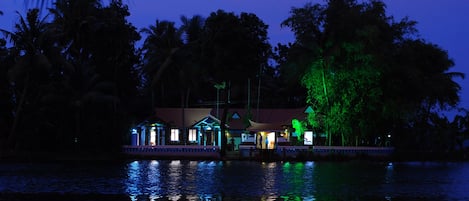 Una casa junto a un lago de noche, con reflejos en el agua.