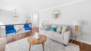 A modern living room with a sofa, two blue chairs, a coffee table, and a decorative mirror.