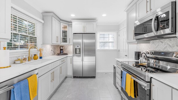 A modern kitchen with white cabinetry, stainless steel appliances, and a marble backsplash.