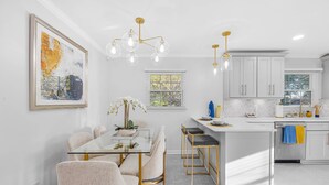 A modern kitchen with white cabinets, a glass dining table, and gold fixtures.
