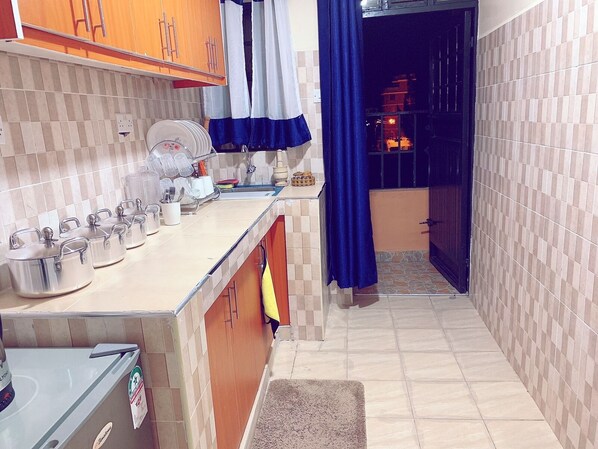 A narrow kitchen with a tiled backsplash, a sink, and a countertop with storage containers.