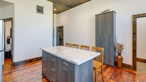 Una cuina amb taulell de marbre, armaris de fusta i zona de menjador amb cadires.