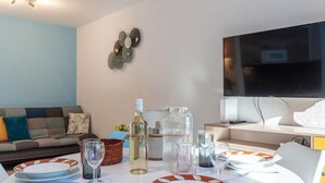 Een moderne woonkamer met een eettafel gedekt voor twee personen, een bank, een televisie en decoratieve wandkunst.