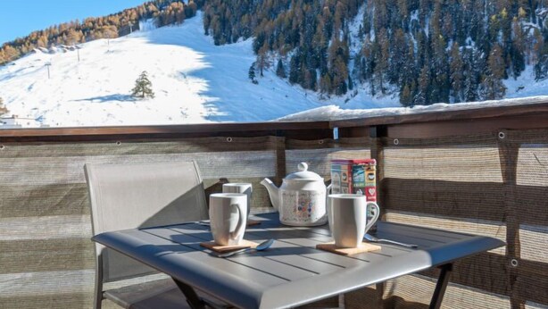 Een balkon met een tafel, twee kopjes en een theepot, met uitzicht op een besneeuwde berg.