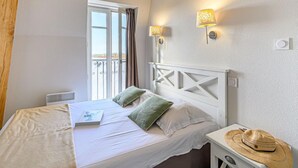 A bedroom with a bed, a window with curtains, two wall-mounted lamps, and a small bedside table with a hat. - Le Château de Kergonano by Interhome (Baden)