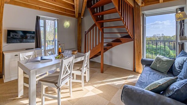 A spacious living area with a wooden staircase, a dining table with chairs, a sofa, and a television. - Le Château de Kergonano by Interhome (Baden)
