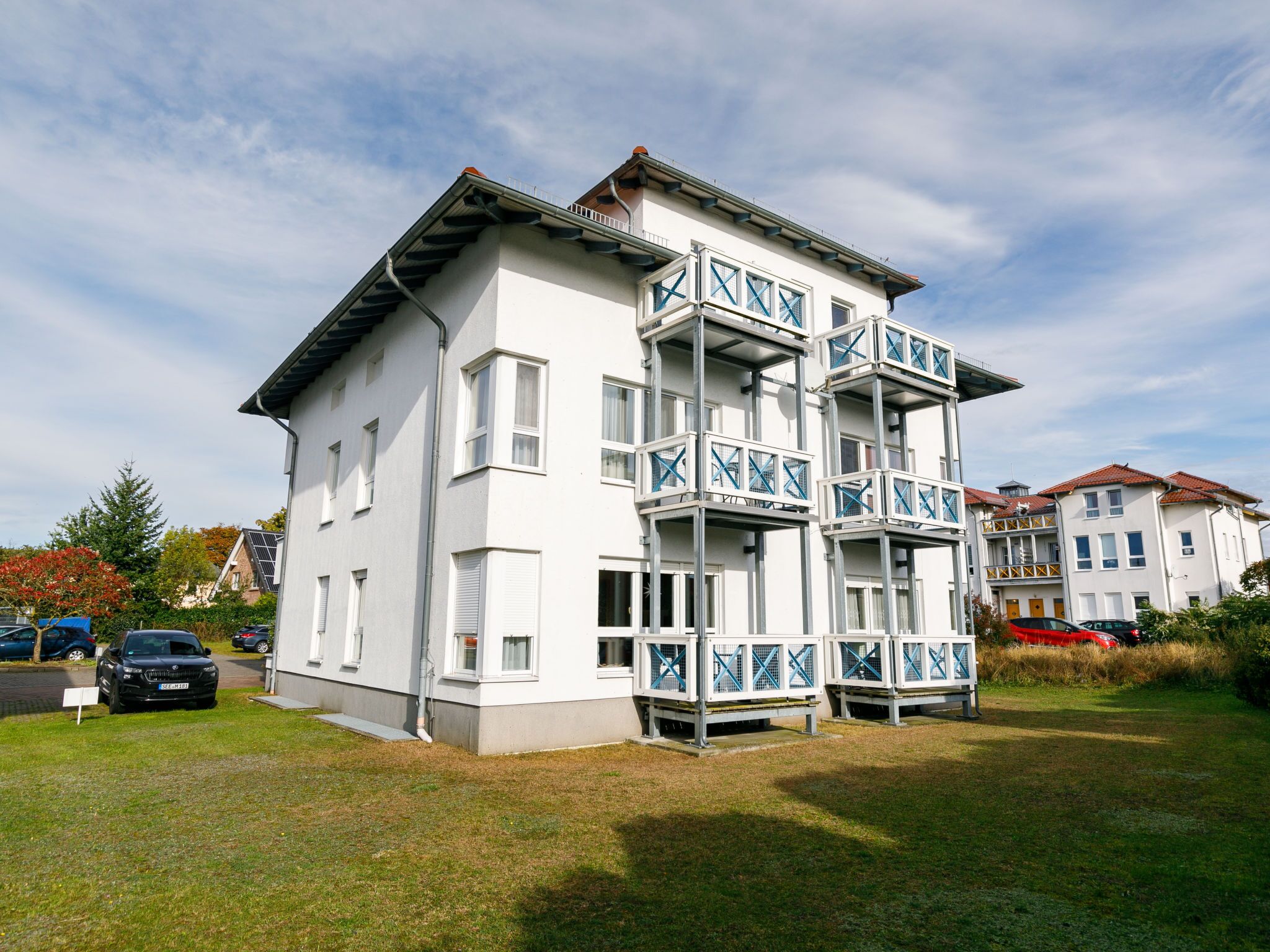 A multi-story residential building with balconies, a flat roof, and a grassy front yard.