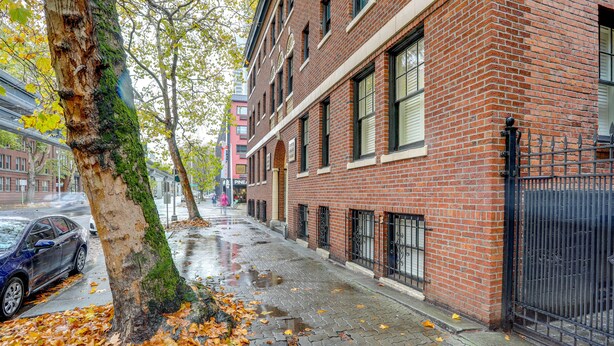 A brick building with a tree in front, a wet sidewalk, and parked cars.