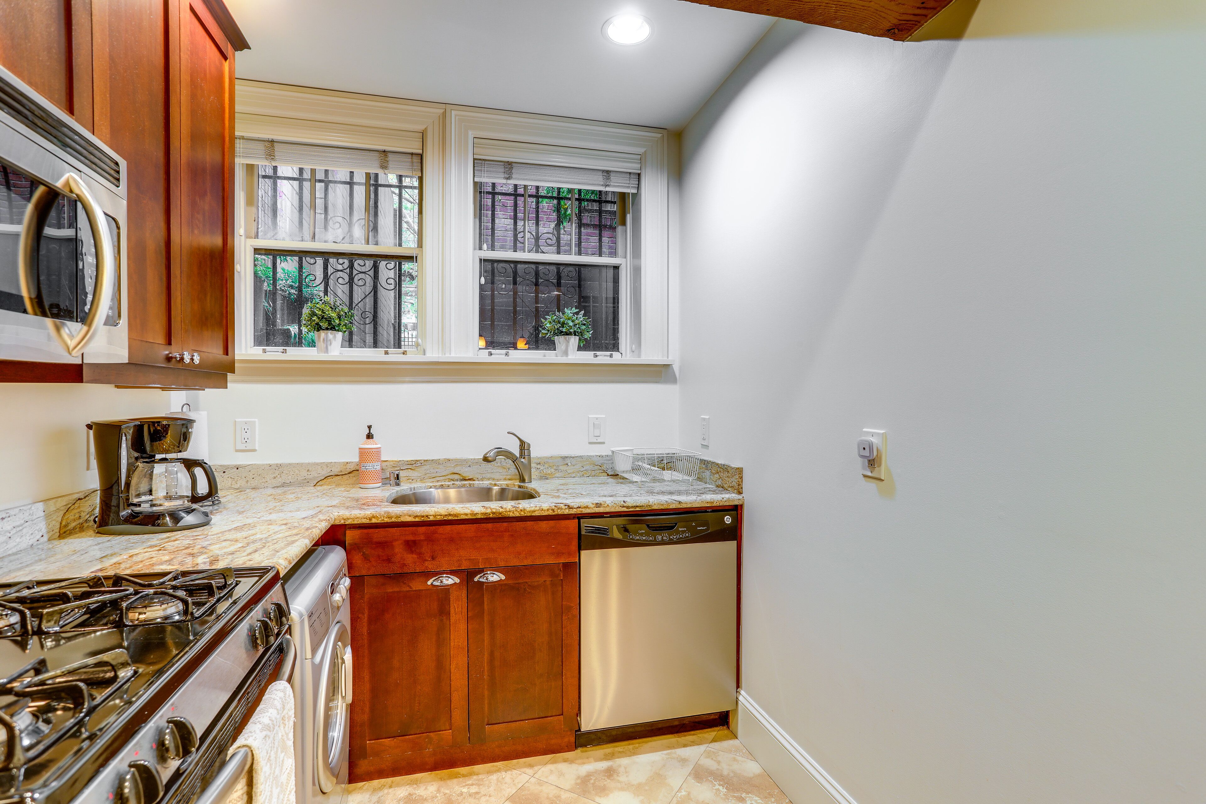 A kitchen with wooden cabinets, a stainless steel stove, a dishwasher, and a window with decorative items.