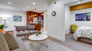 A modern living room with a sofa, armchairs, a coffee table, and a dining area with a kitchen in the background.