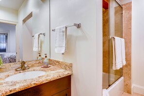 Une salle de bain avec un lavabo en marbre, une cabine de douche en verre et deux serviettes suspendues à des porte-serviettes.