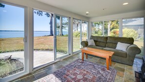 A spacious living area with a large sliding glass door leading to a patio, a green sofa, and a wooden coffee table. - Waterfront Gloucester Cottage w/ Private Boat Dock (Gloucester)
